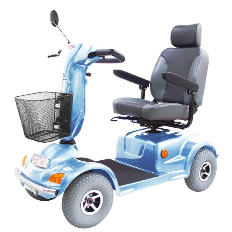 **Alt text:**A light blue mobility scooter with four wheels, featuring a padded gray seat with armrests, a front handlebar with mirror, and a black wire basket, displayed on a plain white background.