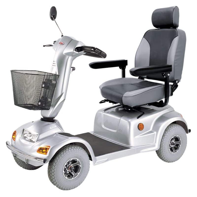 **Alt text:** A silver mobility scooter with four wheels, featuring a padded gray seat with armrests, a front handlebar with mirror, and a wire basket, displayed against a plain white background.